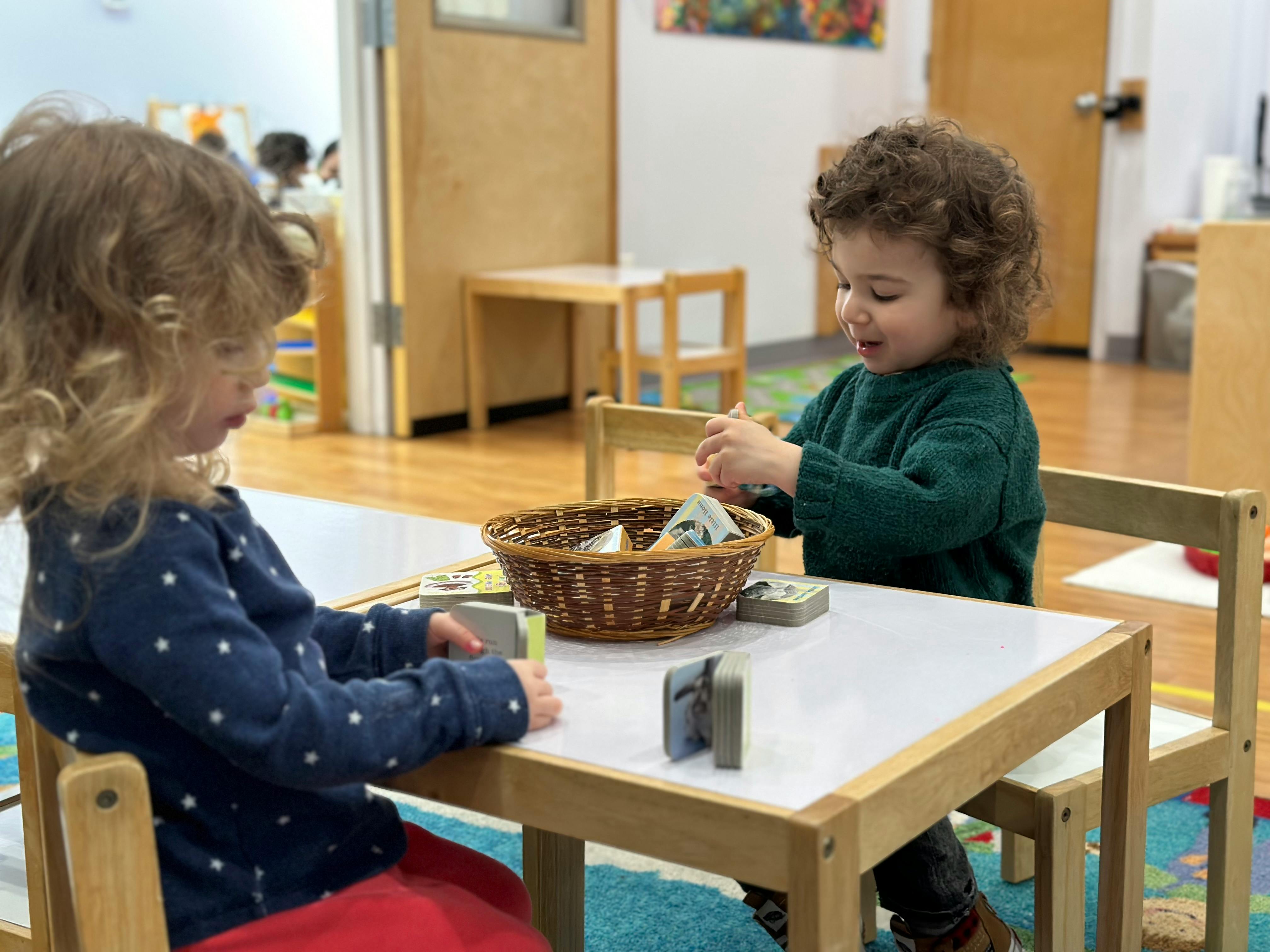 Two children sitting at a table playing with items from a basket