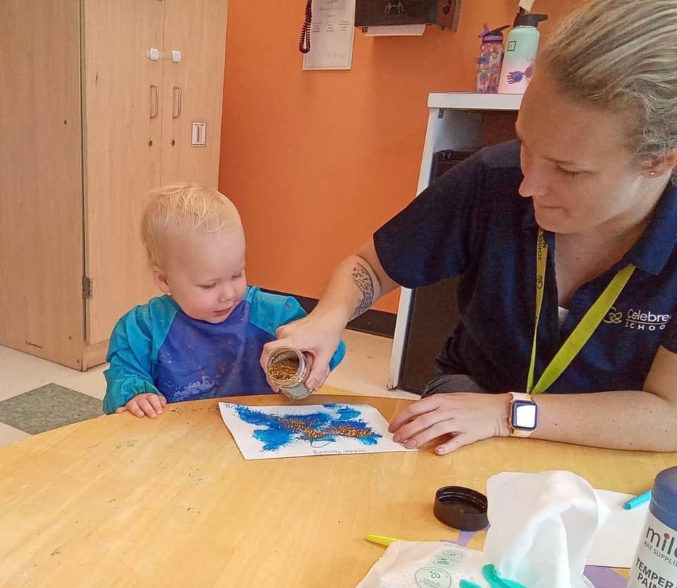 Person helping a child sprinkle glitter on a drawing