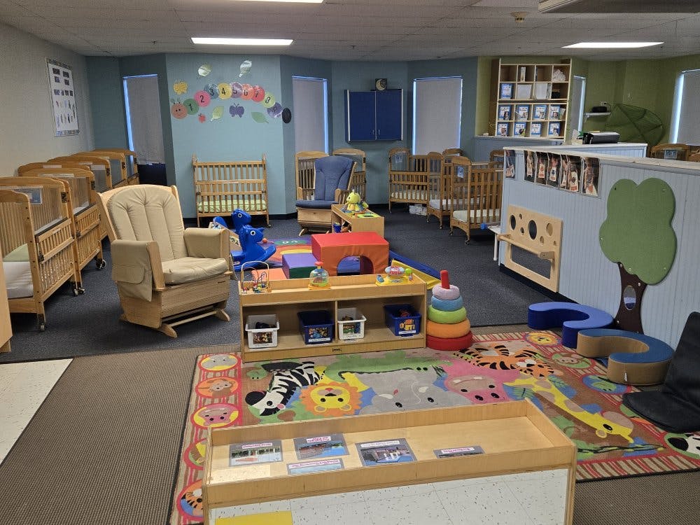 An empty nursery room with cribs, a glider chair, and play mats