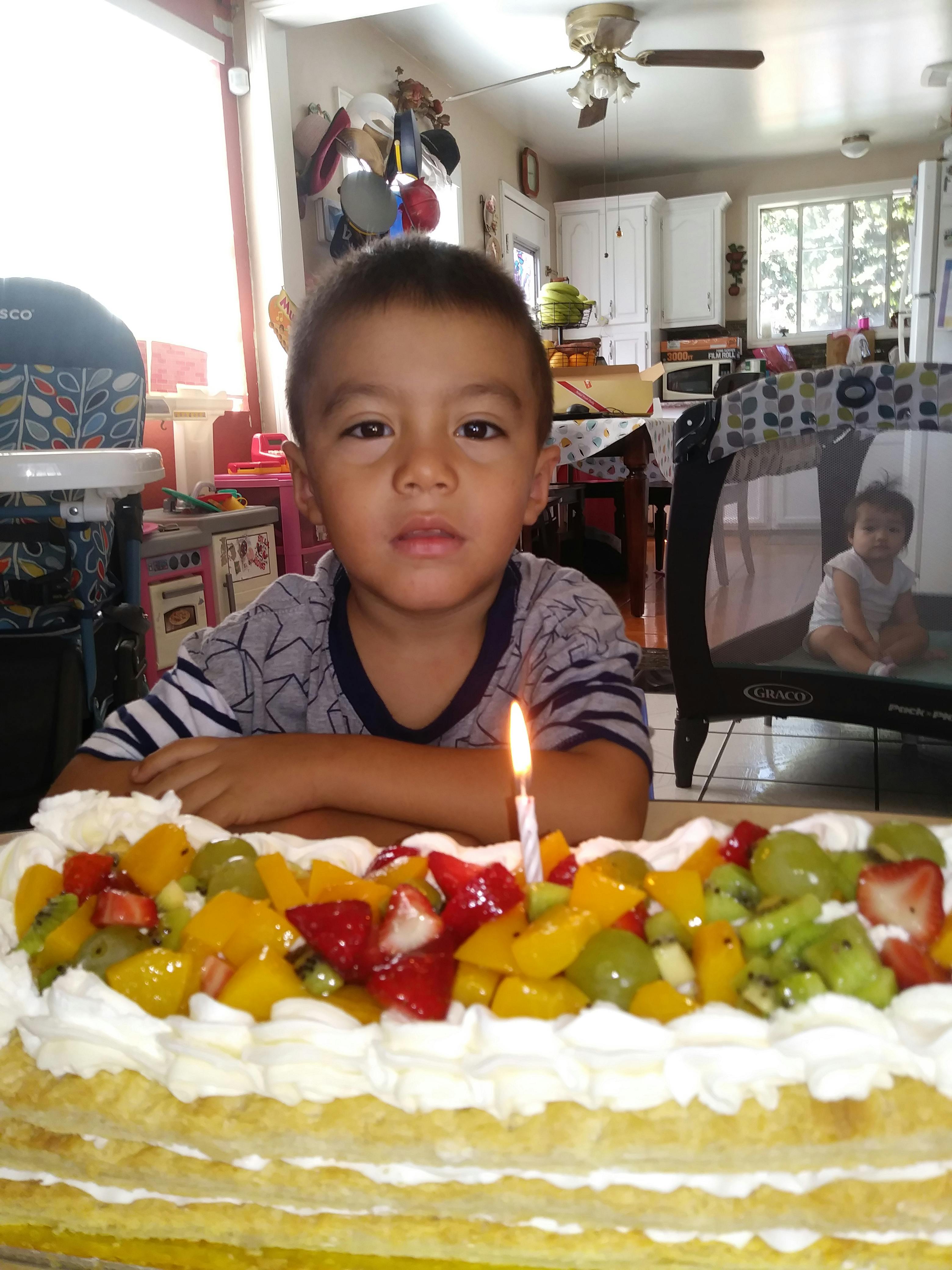 Child sitting behind a fruit-topped cake with a lit candle