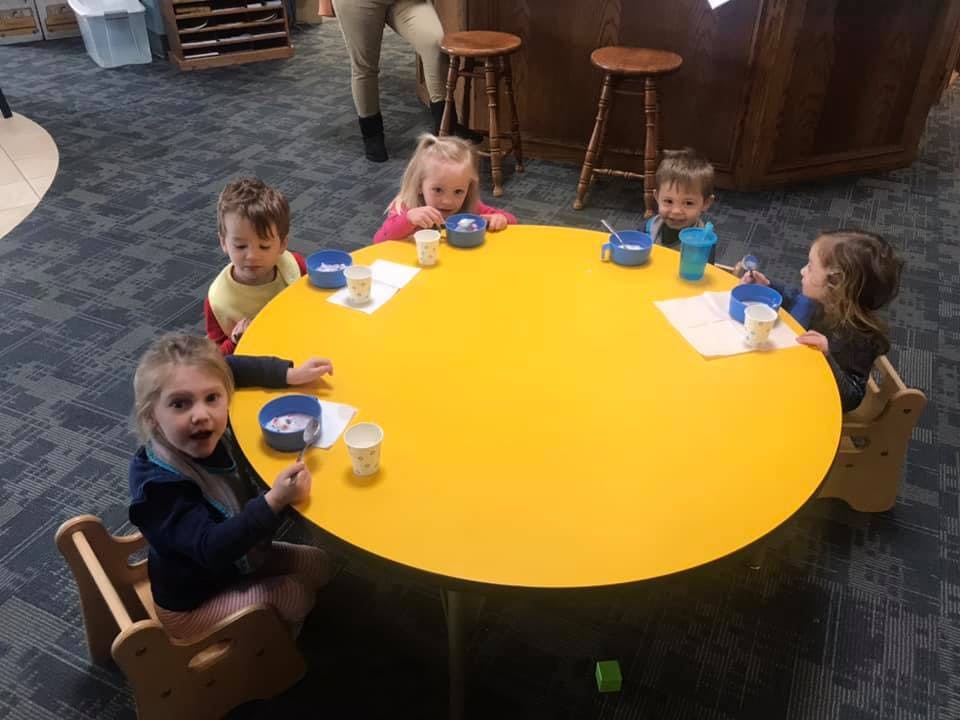 Children sitting around a yellow table with bowls and cups