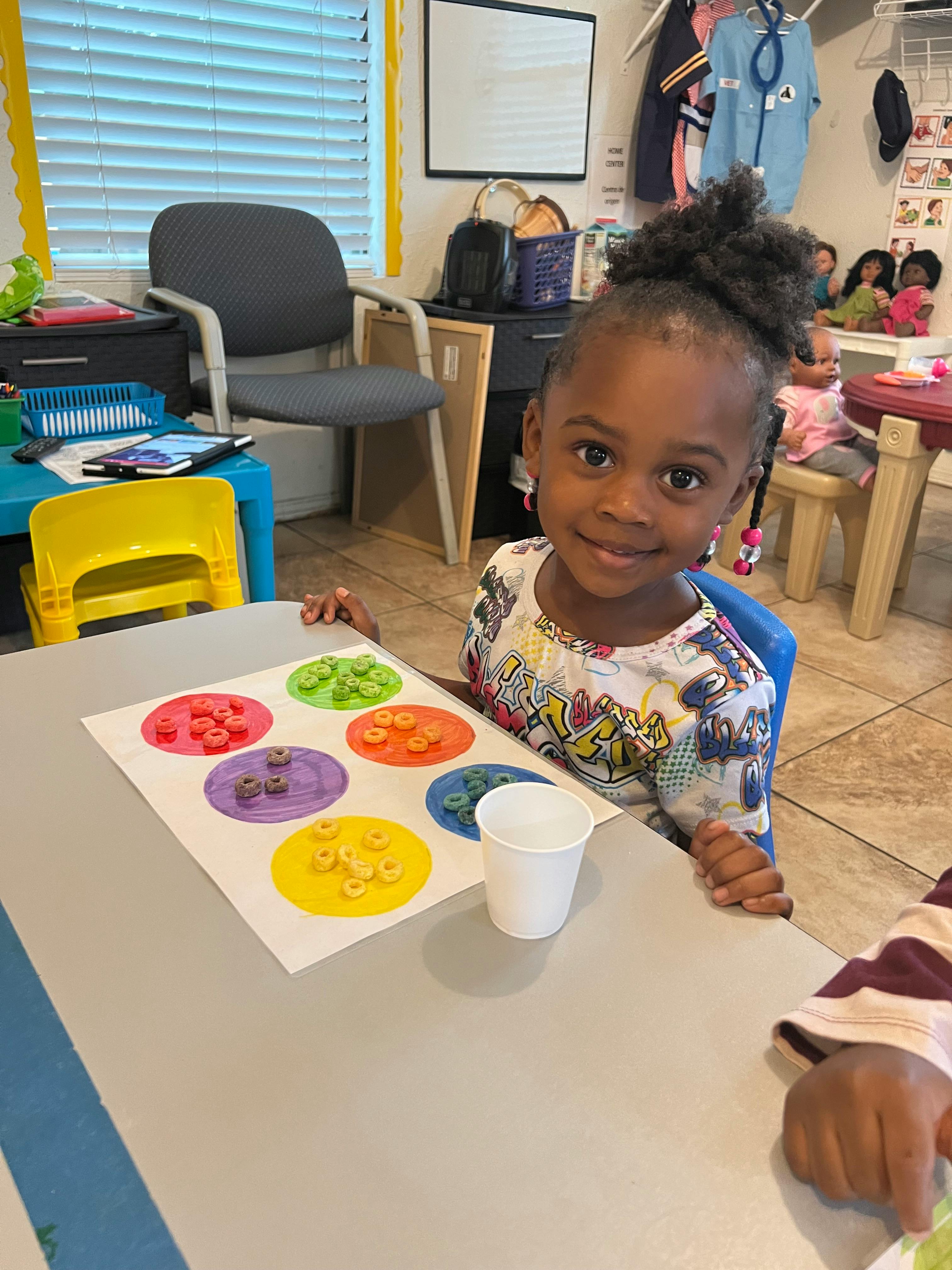Child at a table with a paper showing colorful circles with cereal pieces