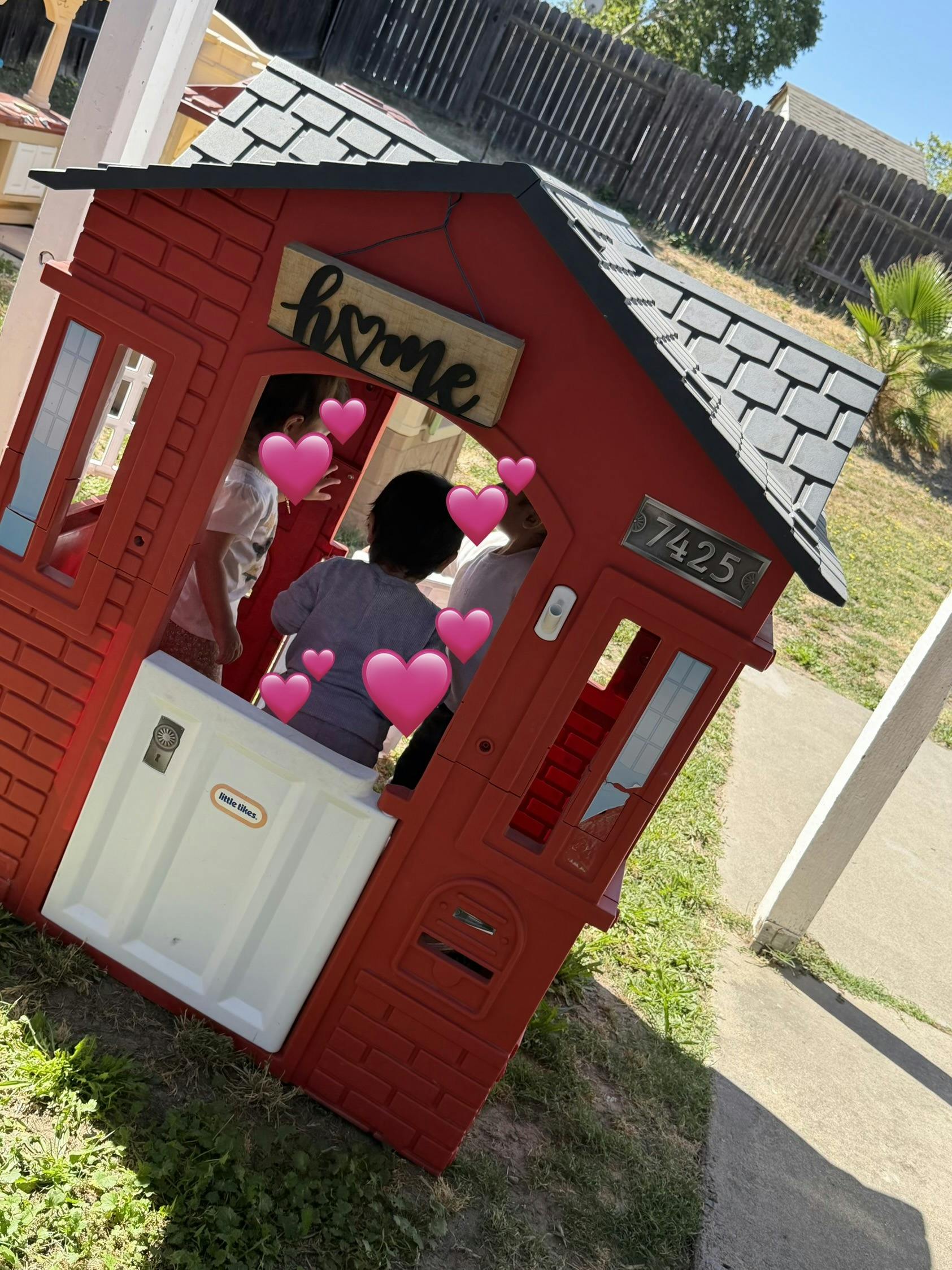 Children playing inside a plastic playhouse with a home sign