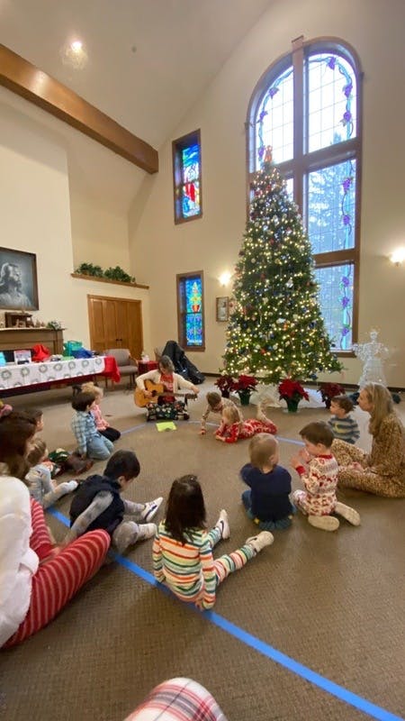 Person playing guitar for children sitting on the floor near a Christmas tree