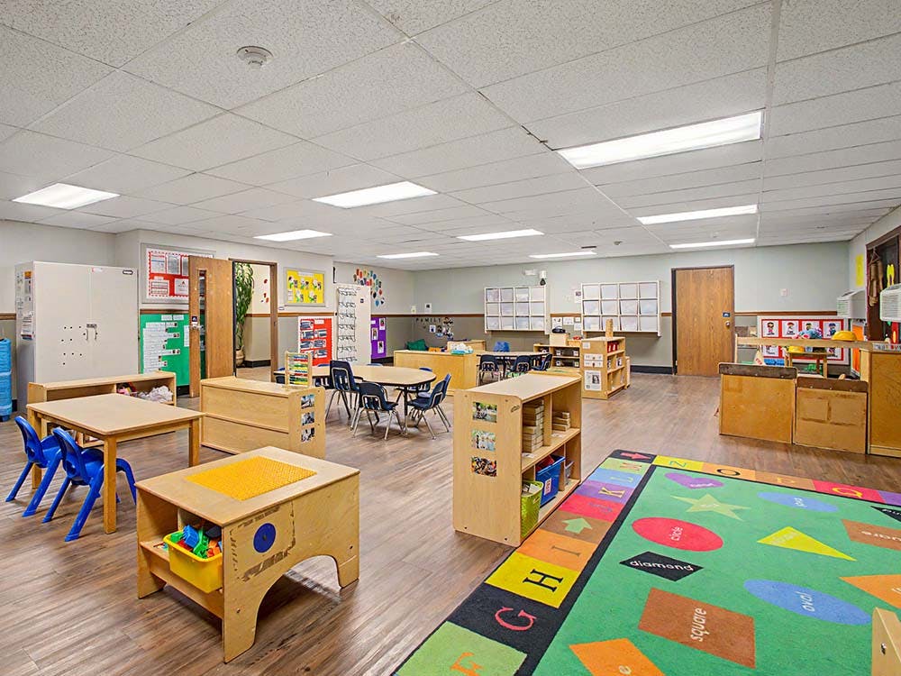 Classroom with small tables, chairs, and a colorful rug with shapes