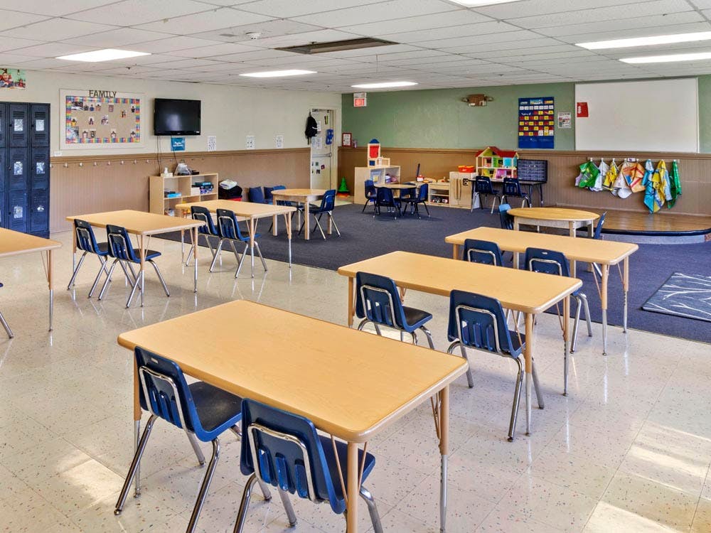 Classroom with child-sized tables and chairs, half carpeted and half tiled floor
