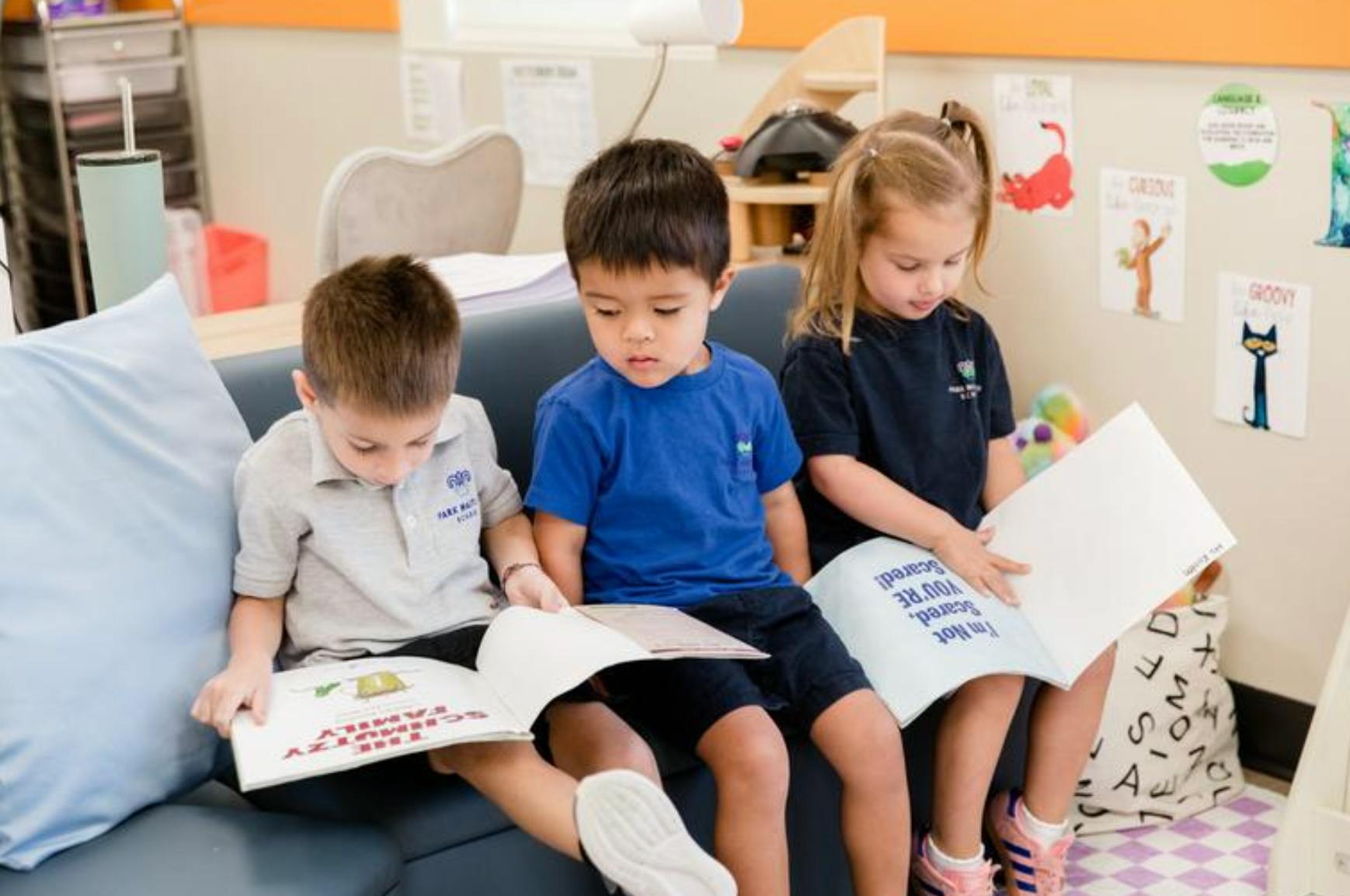 Three children sitting on a couch reading books