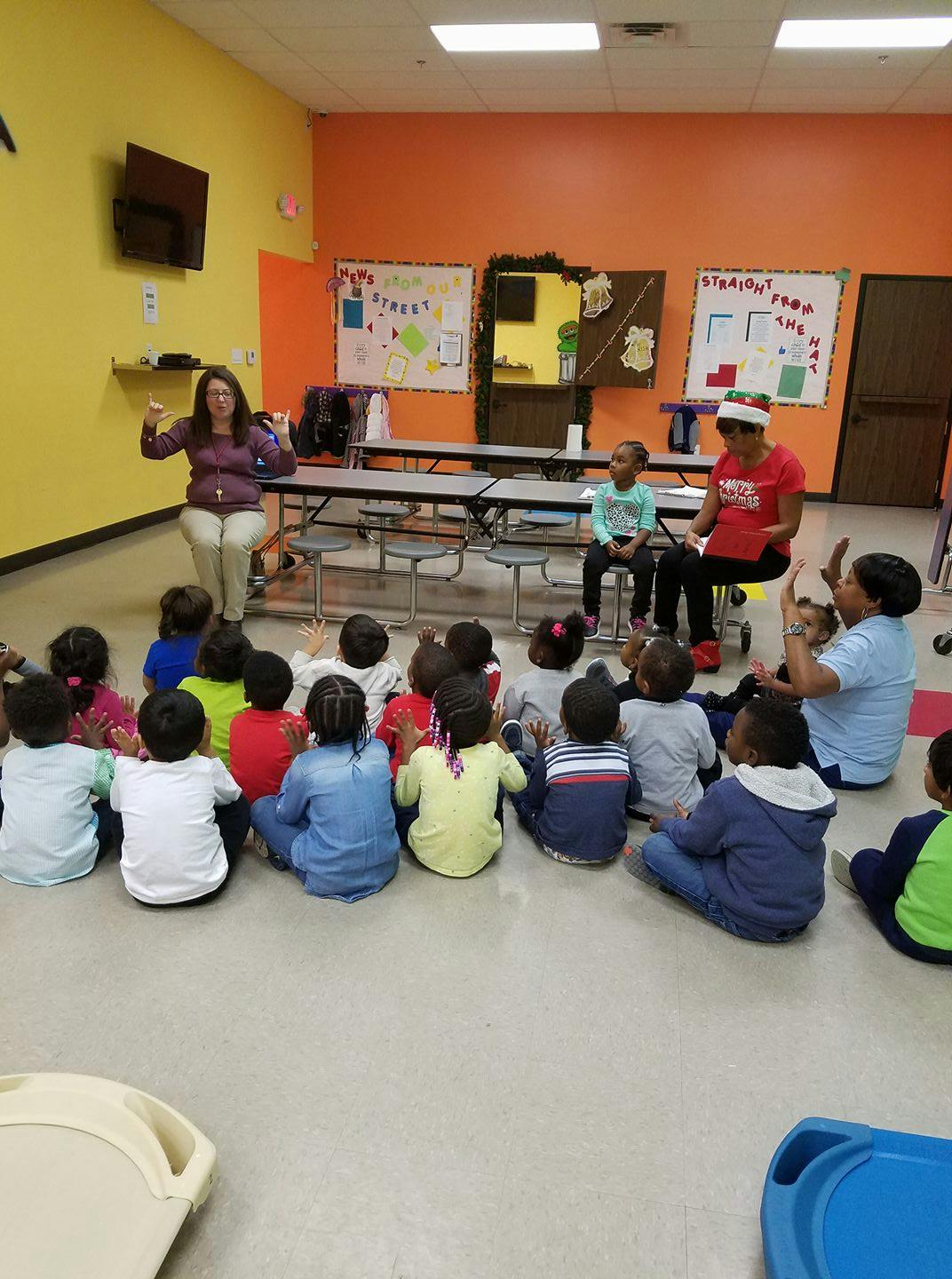 Adults speaking to a group of children sitting on the floor in a classroom