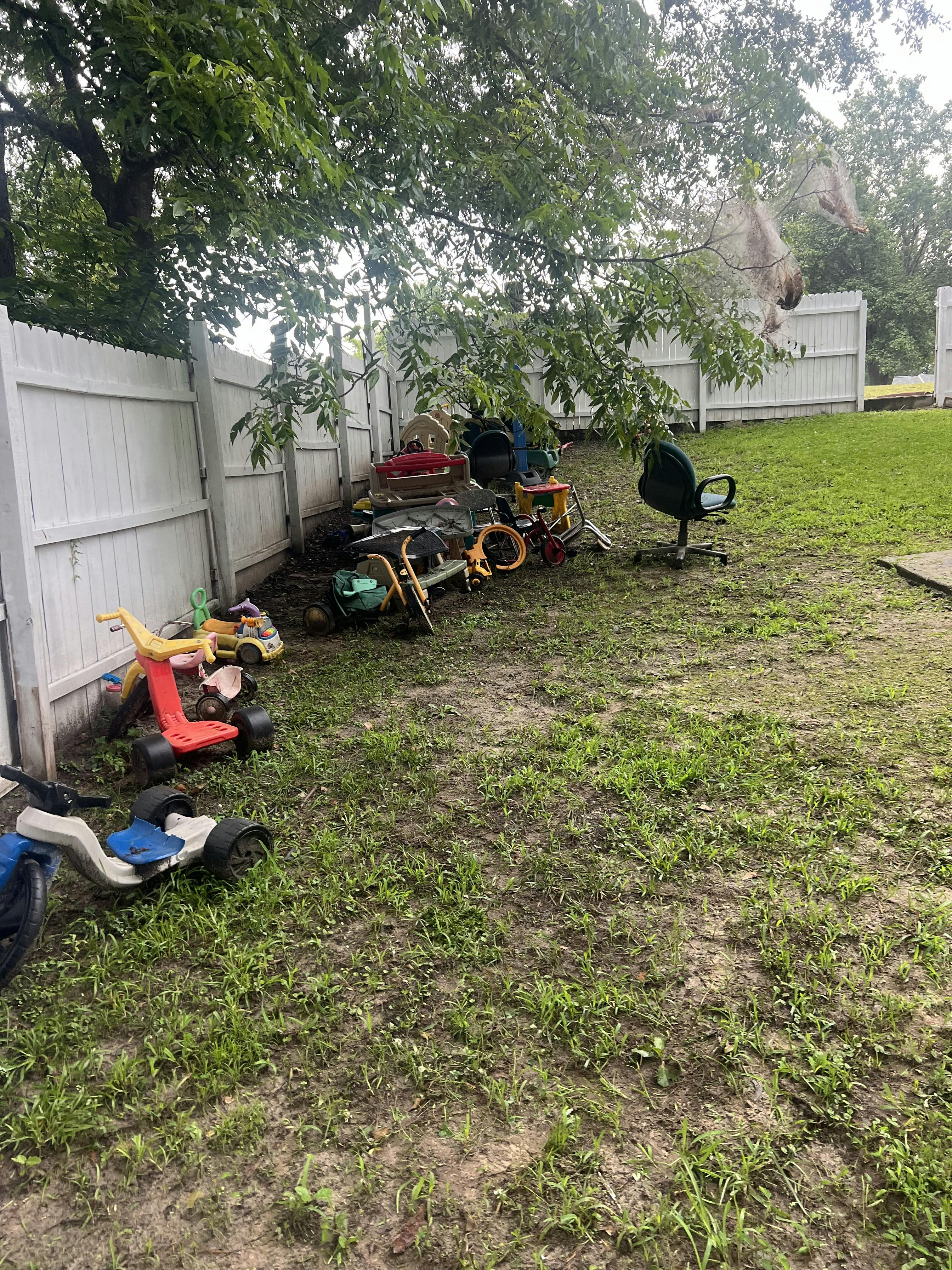 Cluttered backyard with various items piled against a white fence