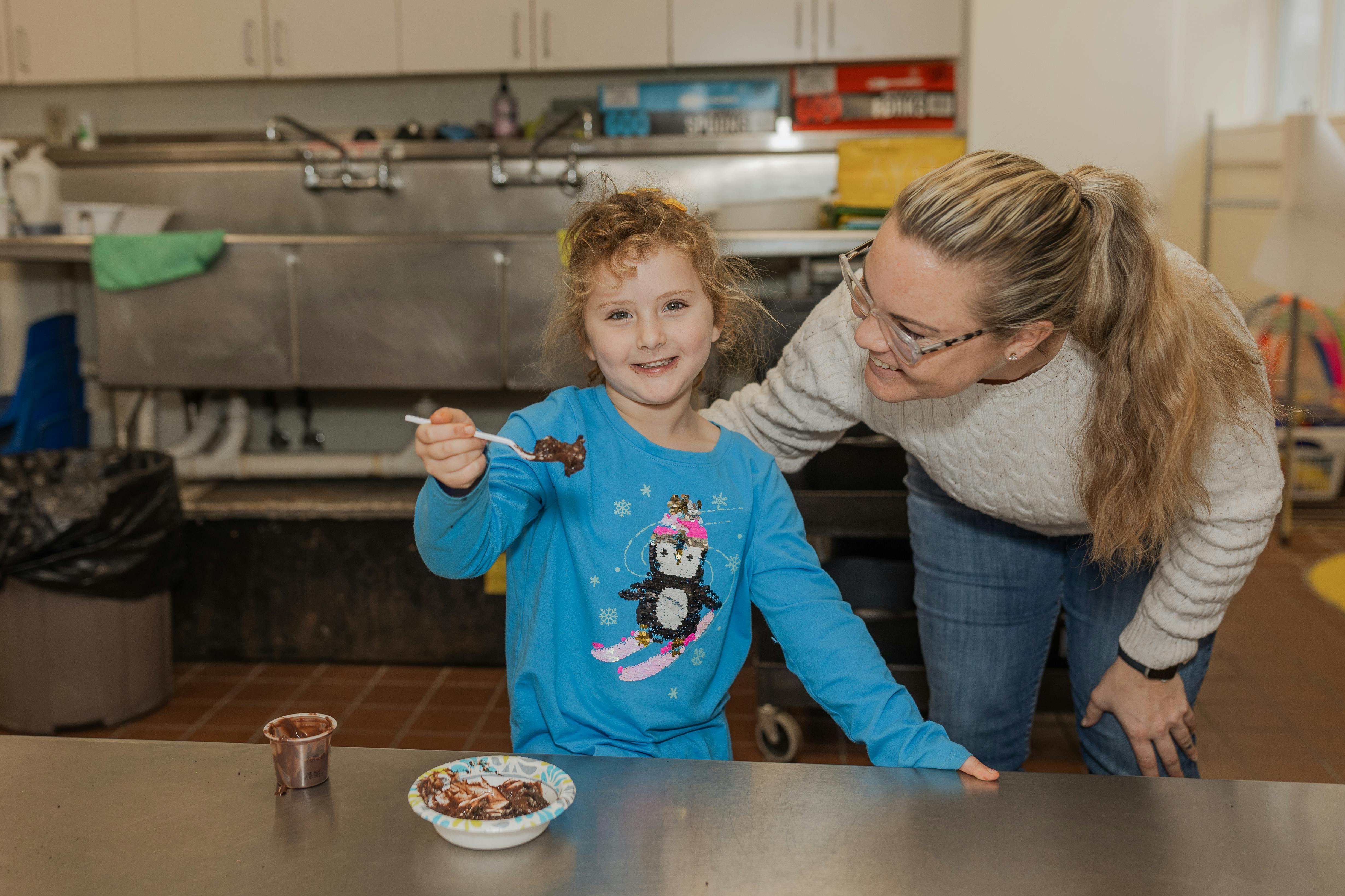 Adult and child in a kitchen, child holding a spoon with food