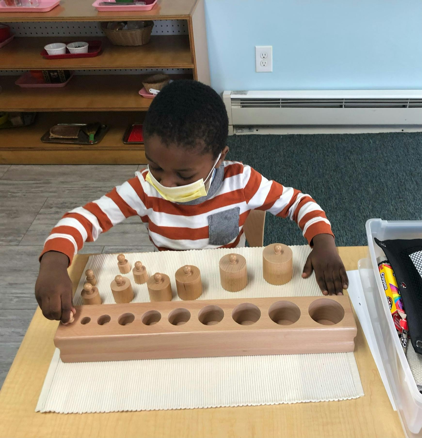 Child in mask playing with wooden cylinder blocks