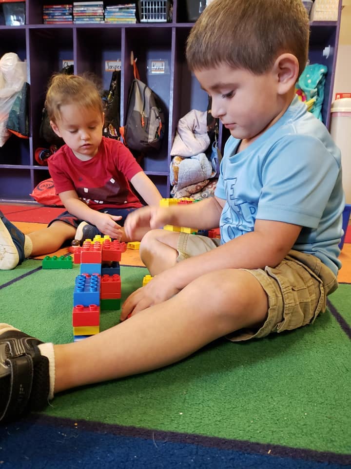 Two children playing with colorful building blocks on a green rug