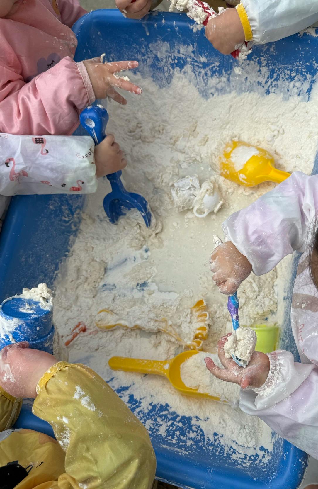Children playing with flour and sand toys in a blue bin