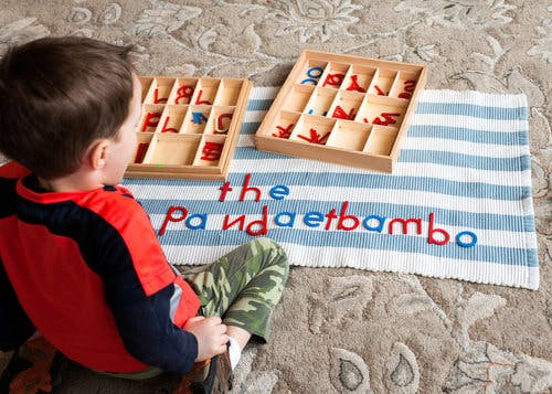 Child sitting on floor with letter tiles and a mat with a striped mat