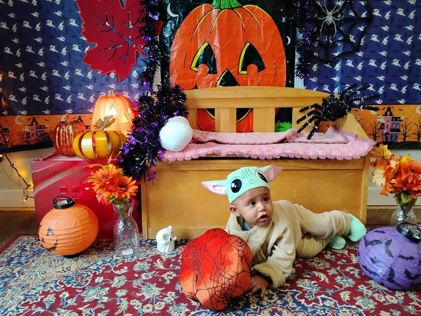 Child in a costume crawling on a rug with Halloween decorations