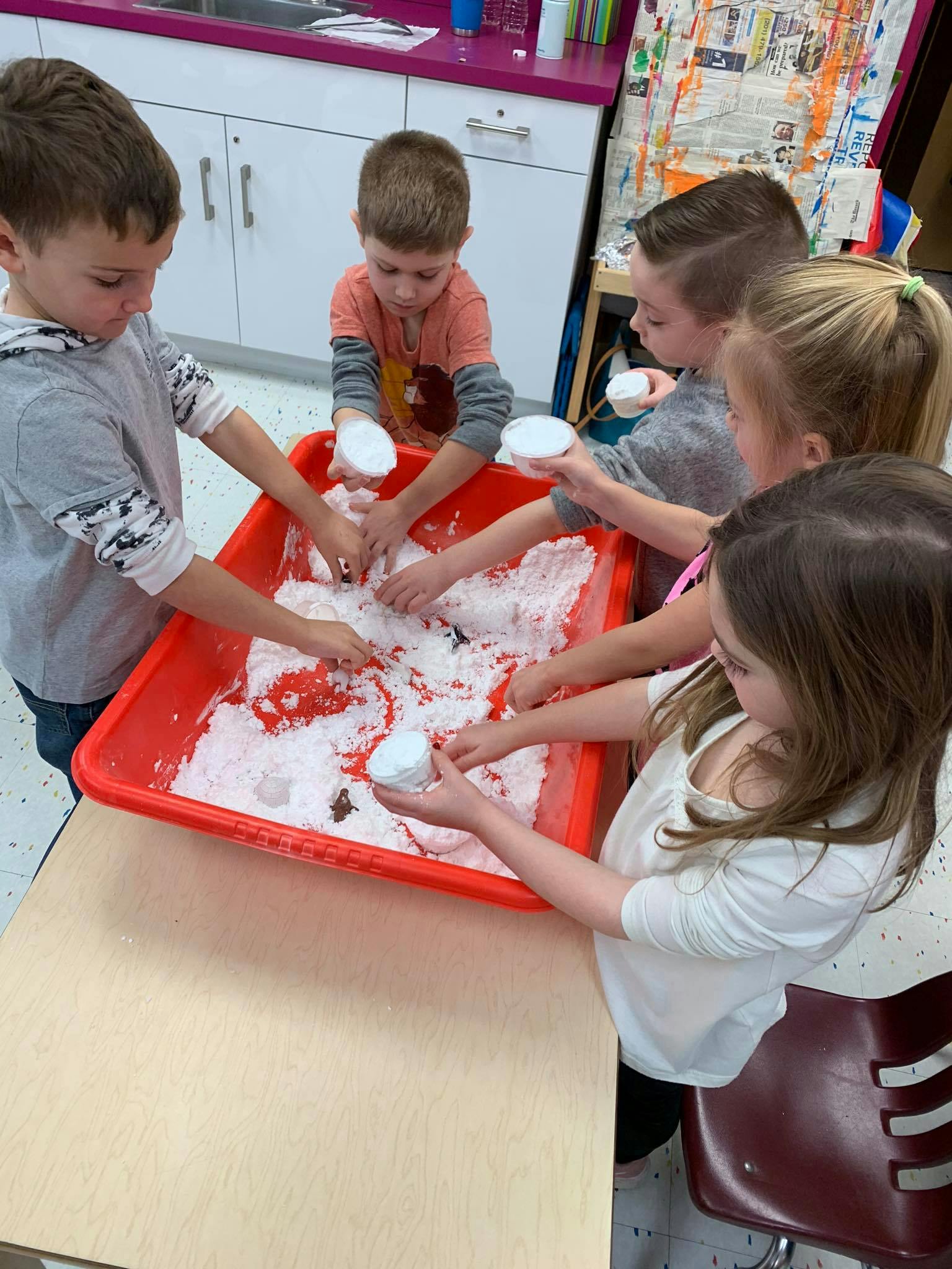 Children playing with white material in a red bin