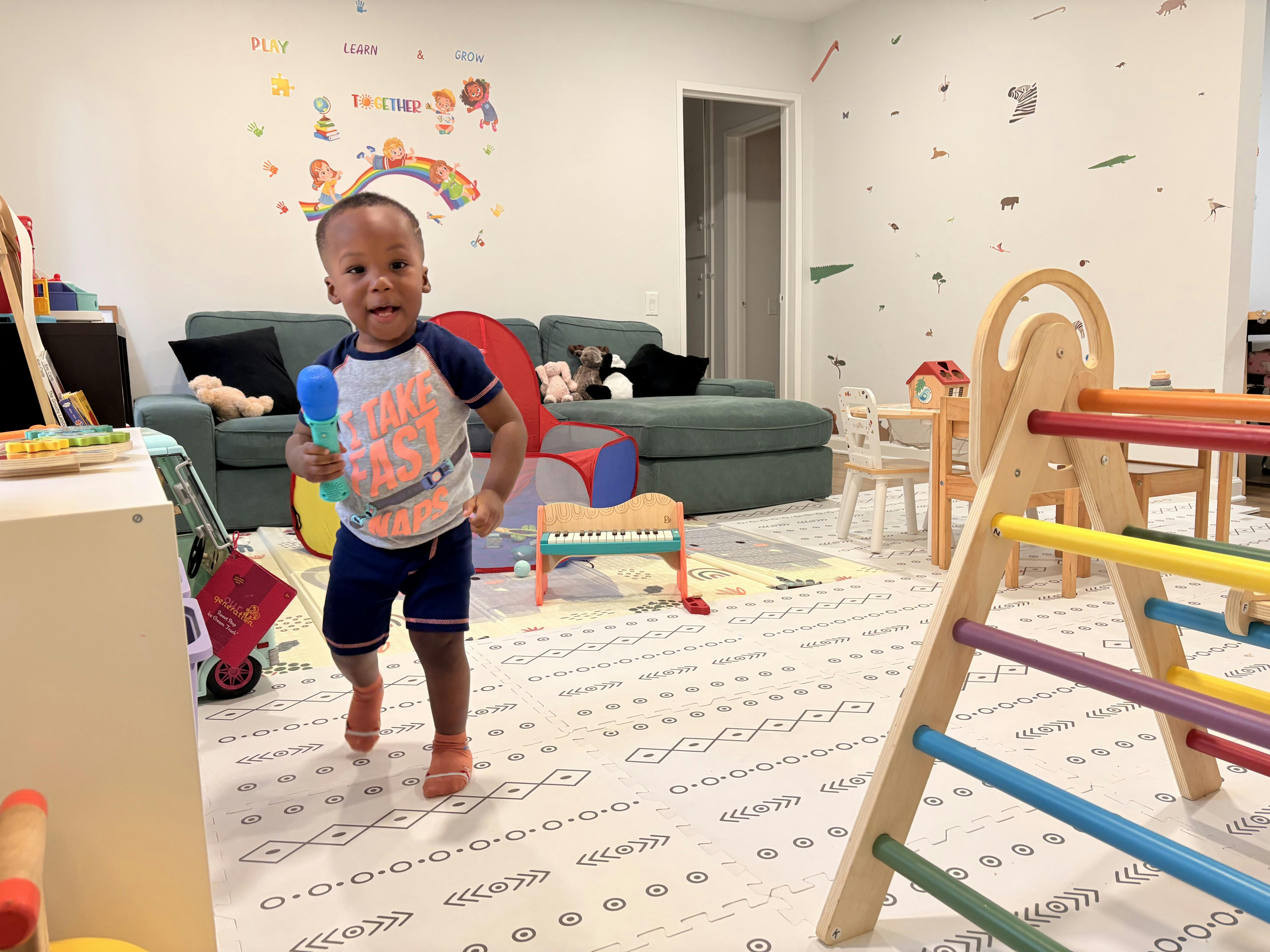 Child walking and holding a toy microphone in a playroom