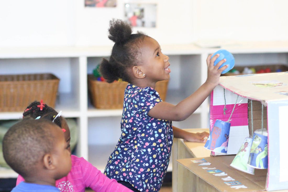 Child playing with a blue ball and a toy house