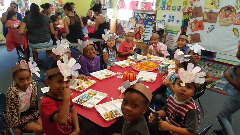 Children wearing paper turkey hats sitting at a table with food