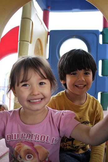 Two children smiling at the camera on a playground