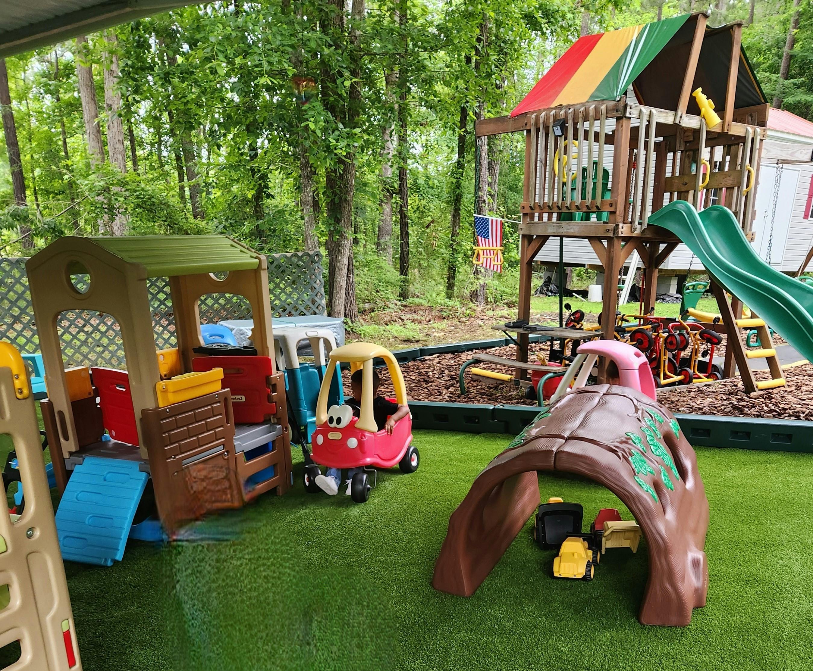 Outdoor playground with playhouses, slides, and ride-on toys on artificial turf