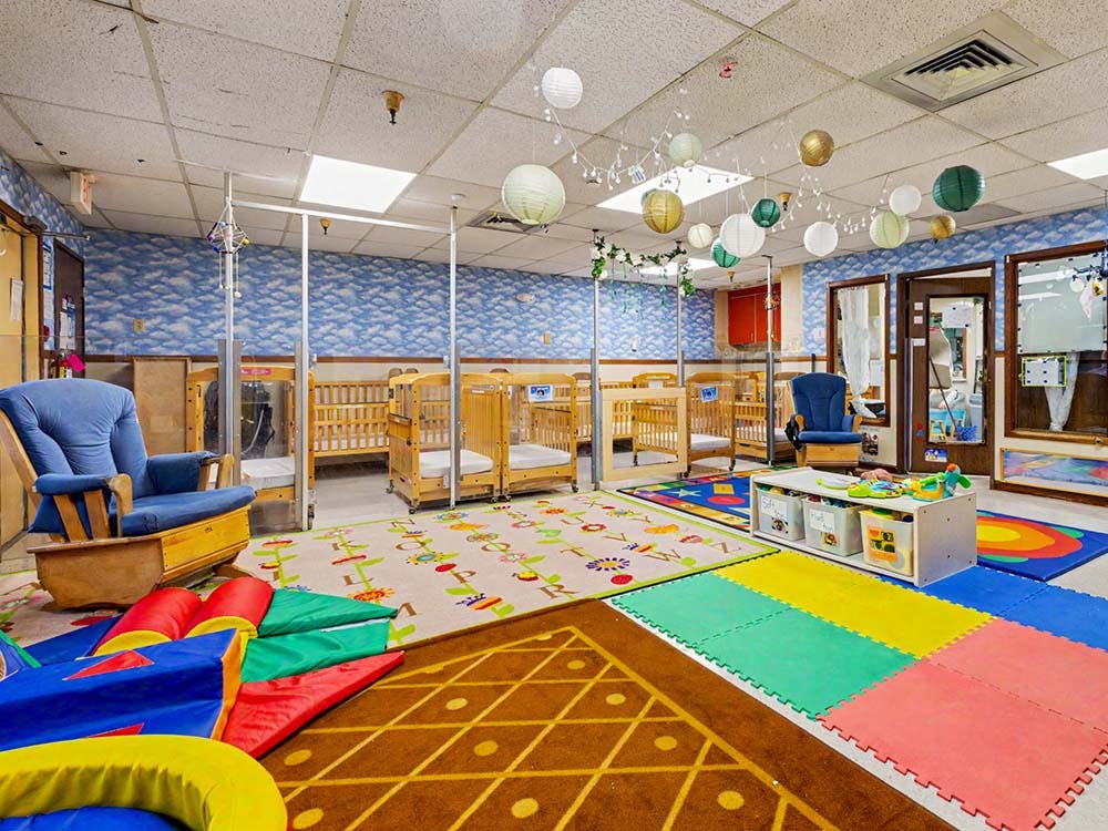 A colorful room with cribs, chairs, playmats, and paper lanterns