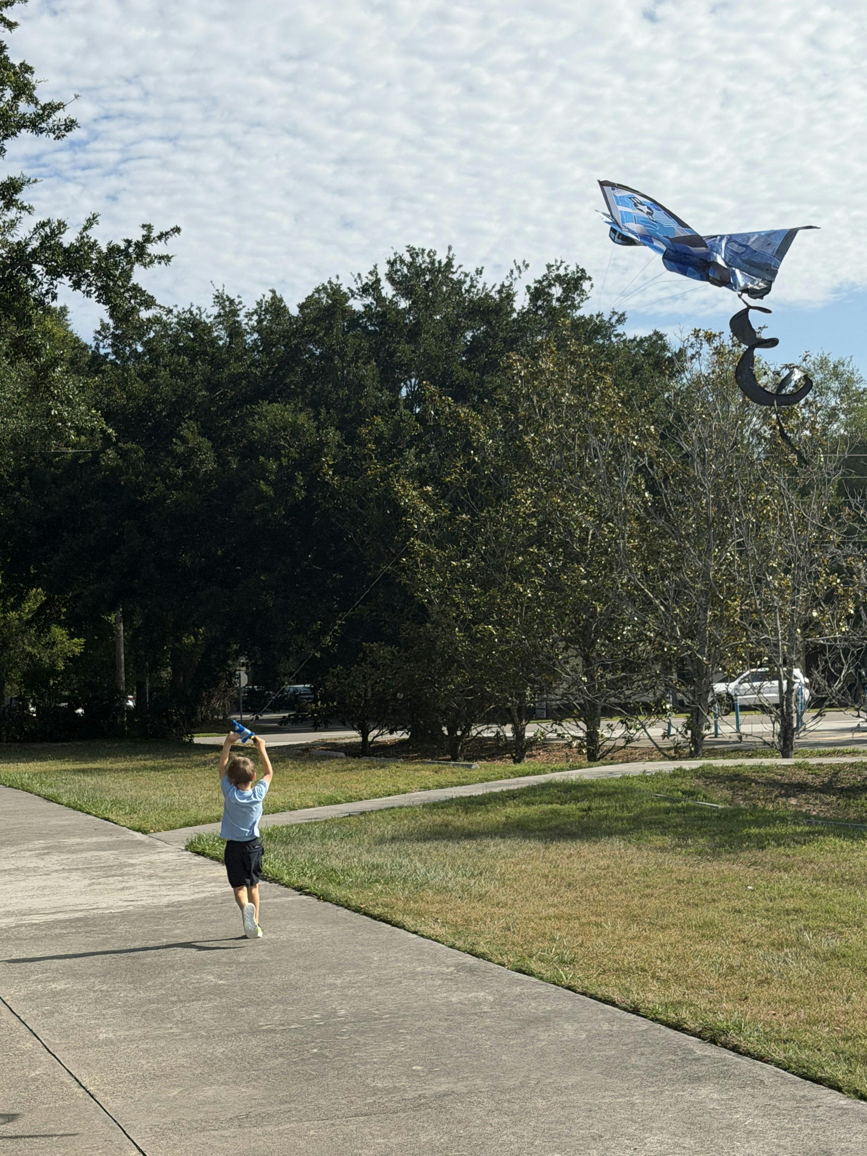 Child running with a small object in their hands, a kite flying above