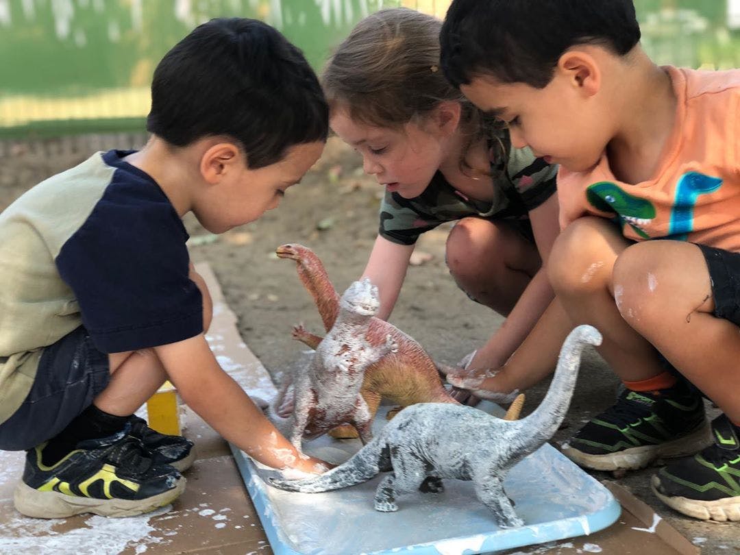 Three children playing with dinosaur toys covered in white powder