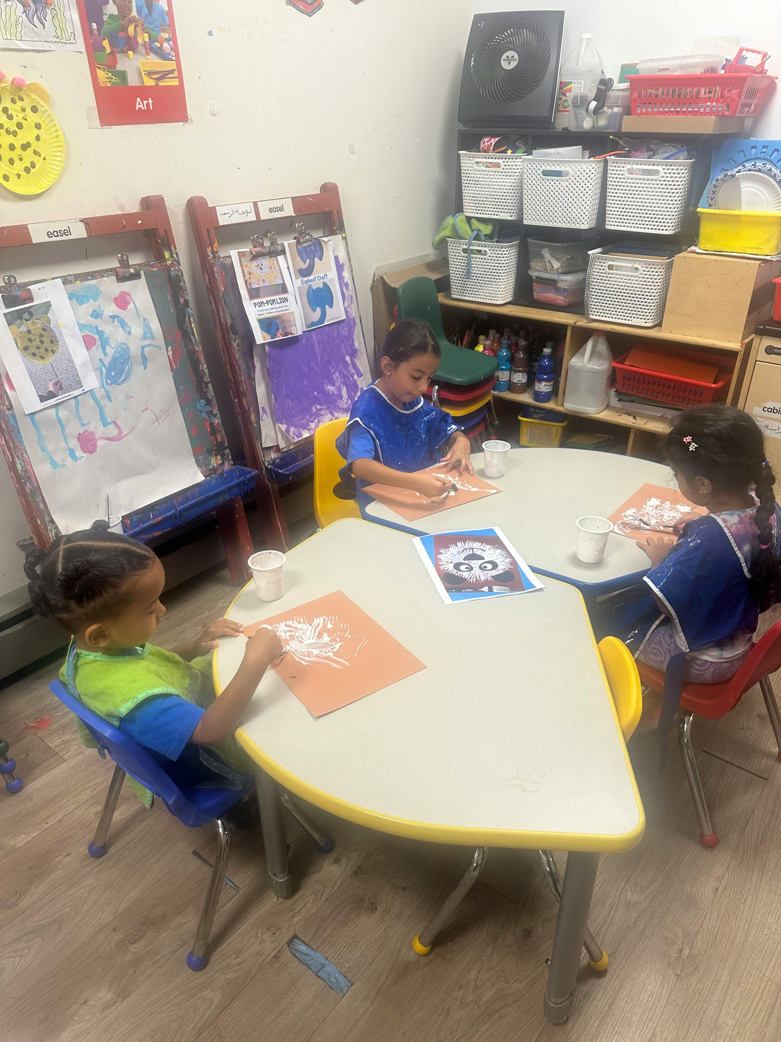Three children sitting at tables doing crafts