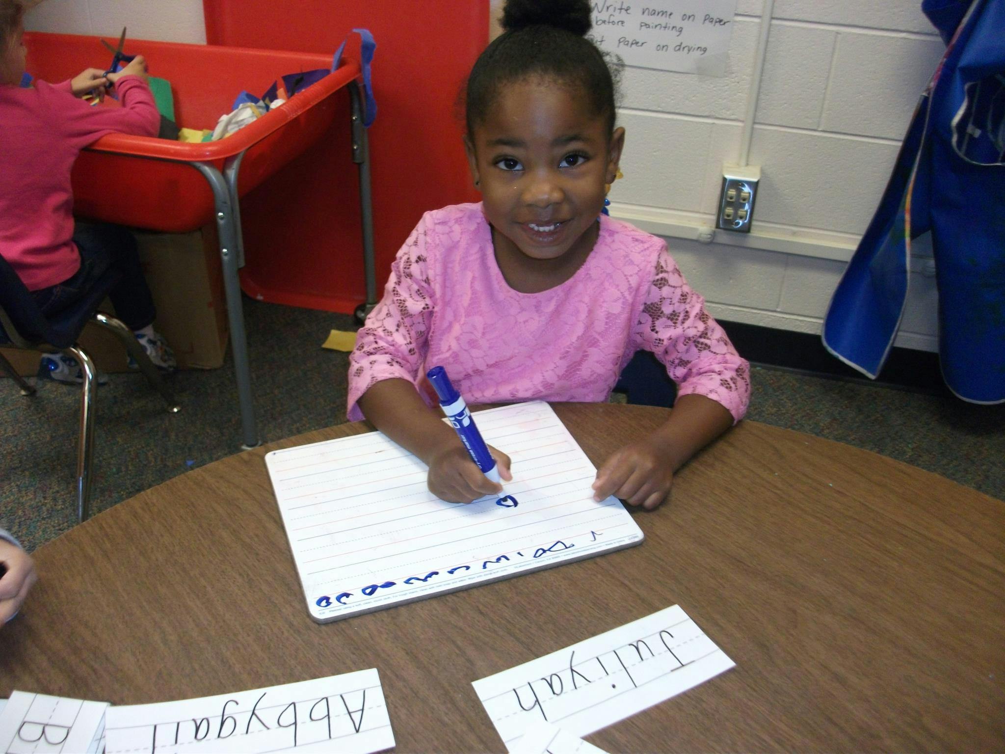 Child writing on a whiteboard with a blue marker in a classroom