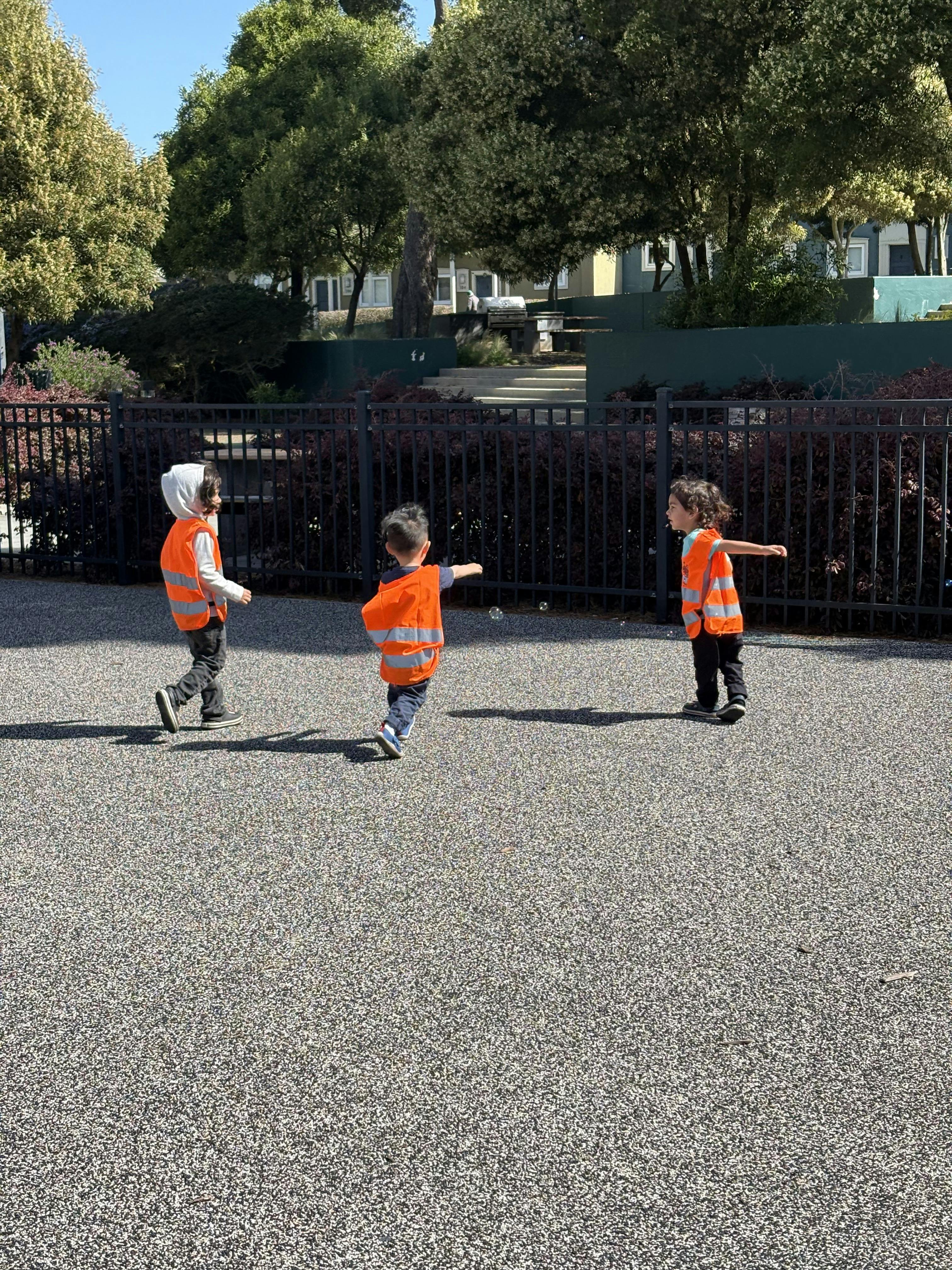 Three children in orange vests playing outdoors
