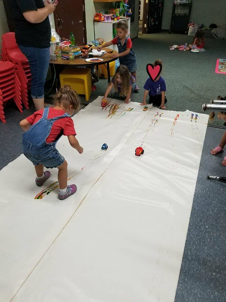 Children playing with toy cars on a large sheet of paper