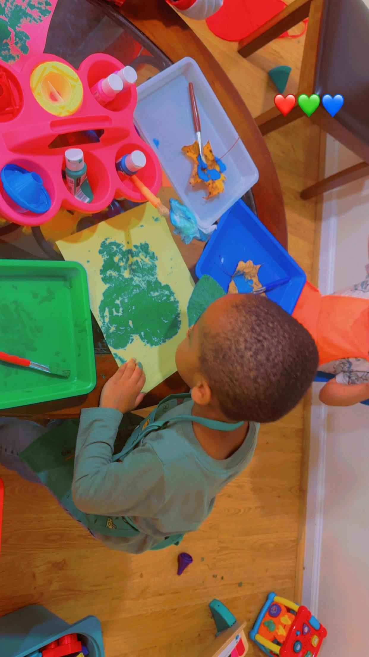 Child painting a green image on yellow paper at a table