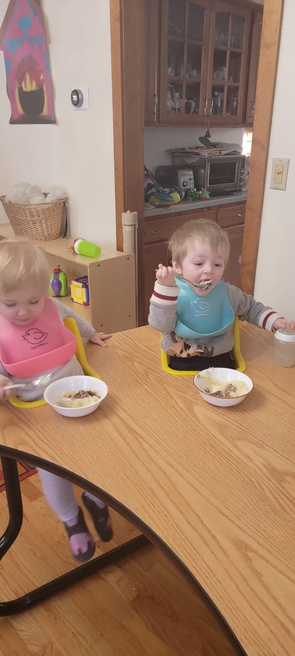 Two children in bibs eating from bowls at a table
