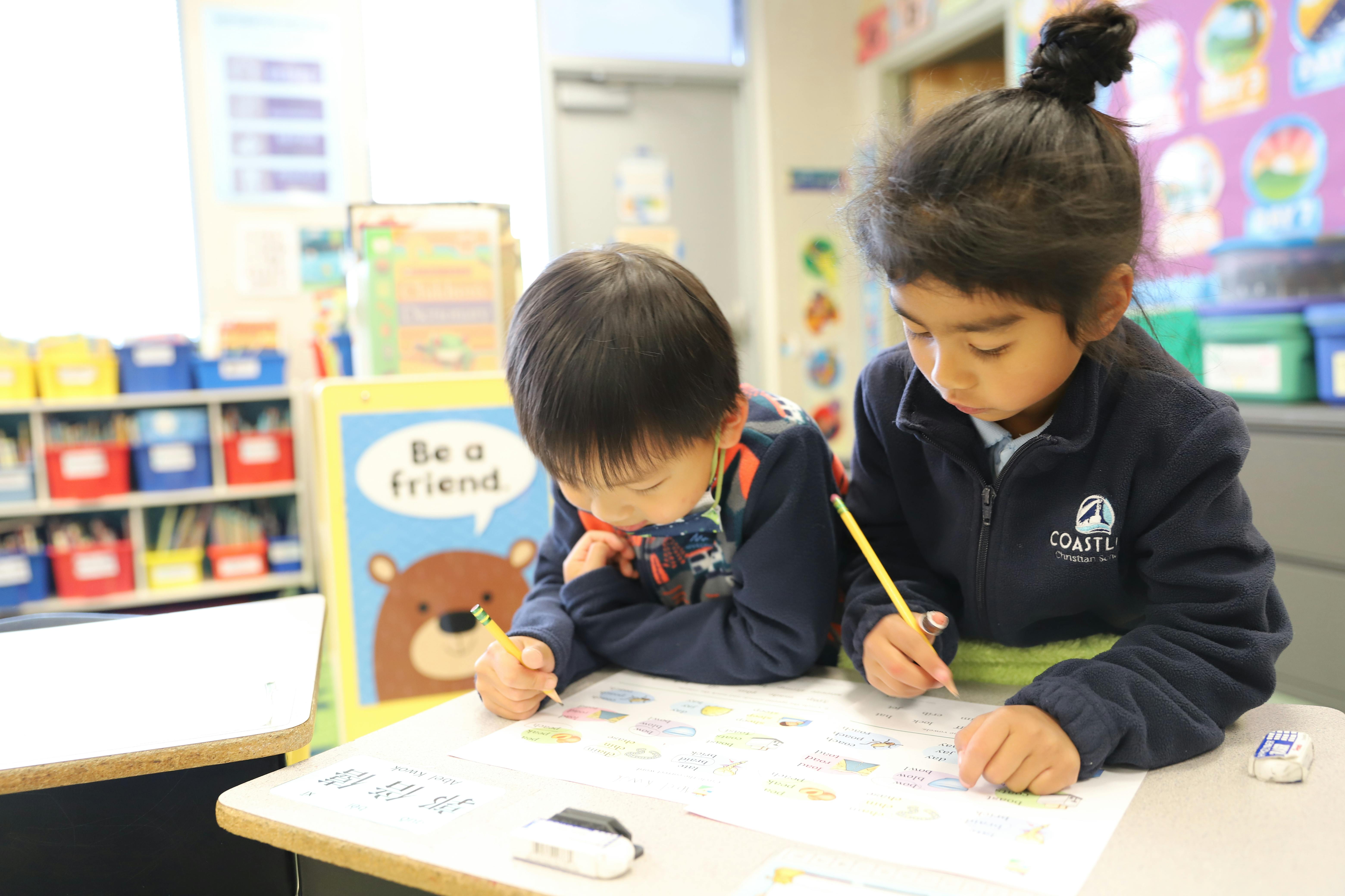 Two children writing at a desk in a classroom