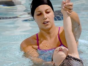 Person in swim cap helping child in pool