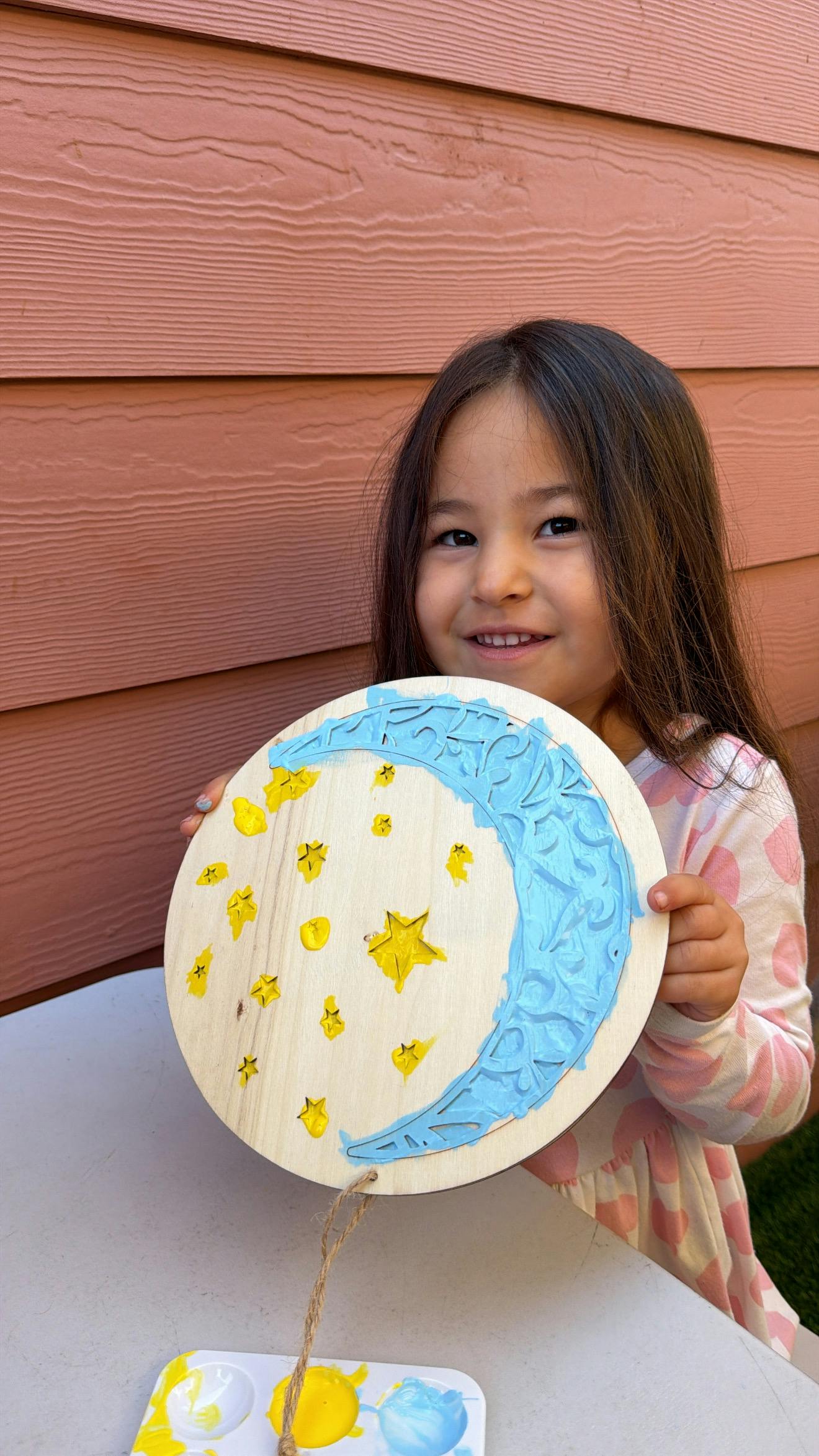 Child holding a round wooden sign decorated with a painted blue moon and stars