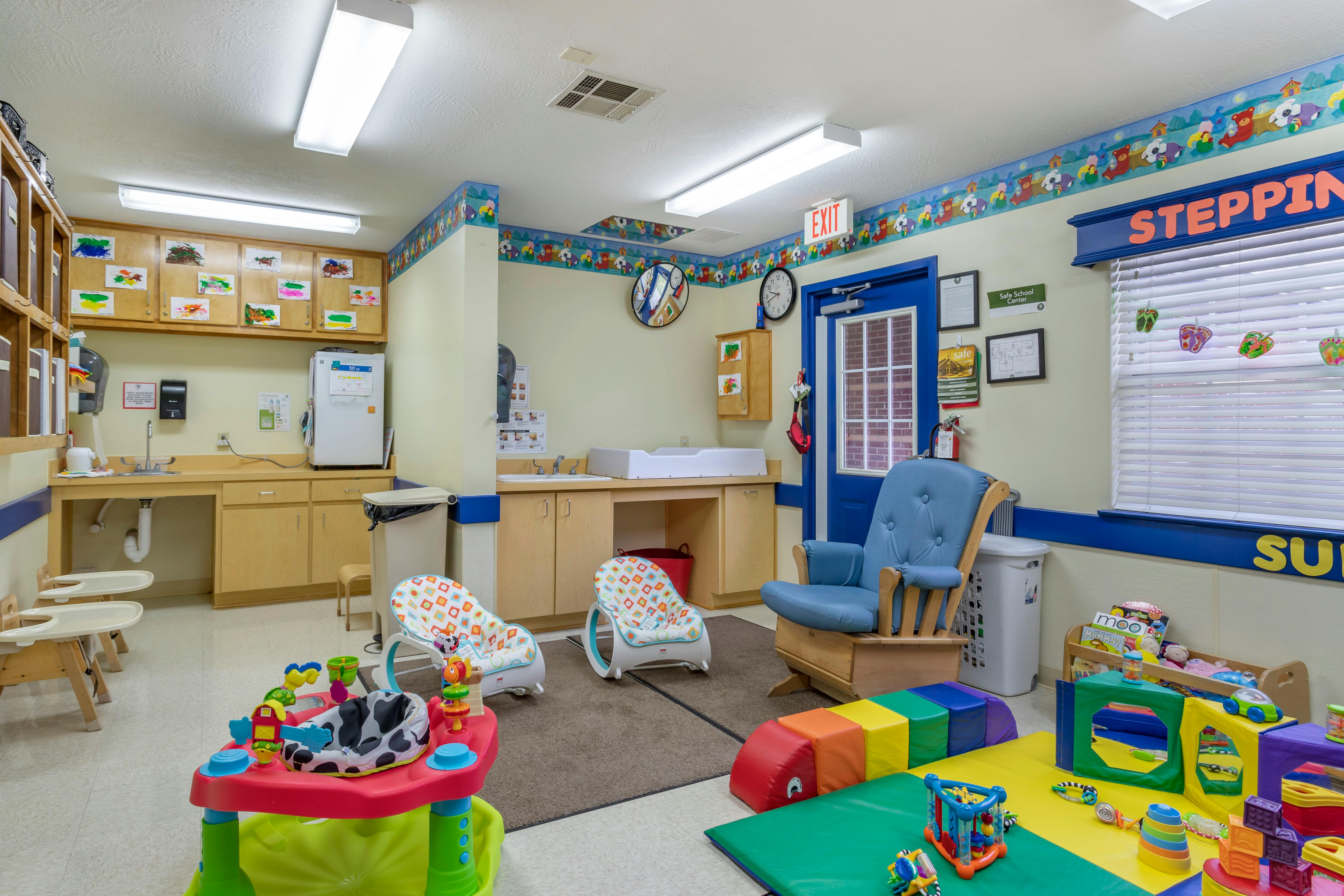 Childcare room with a changing station, baby rockers, infant seats, and play mats