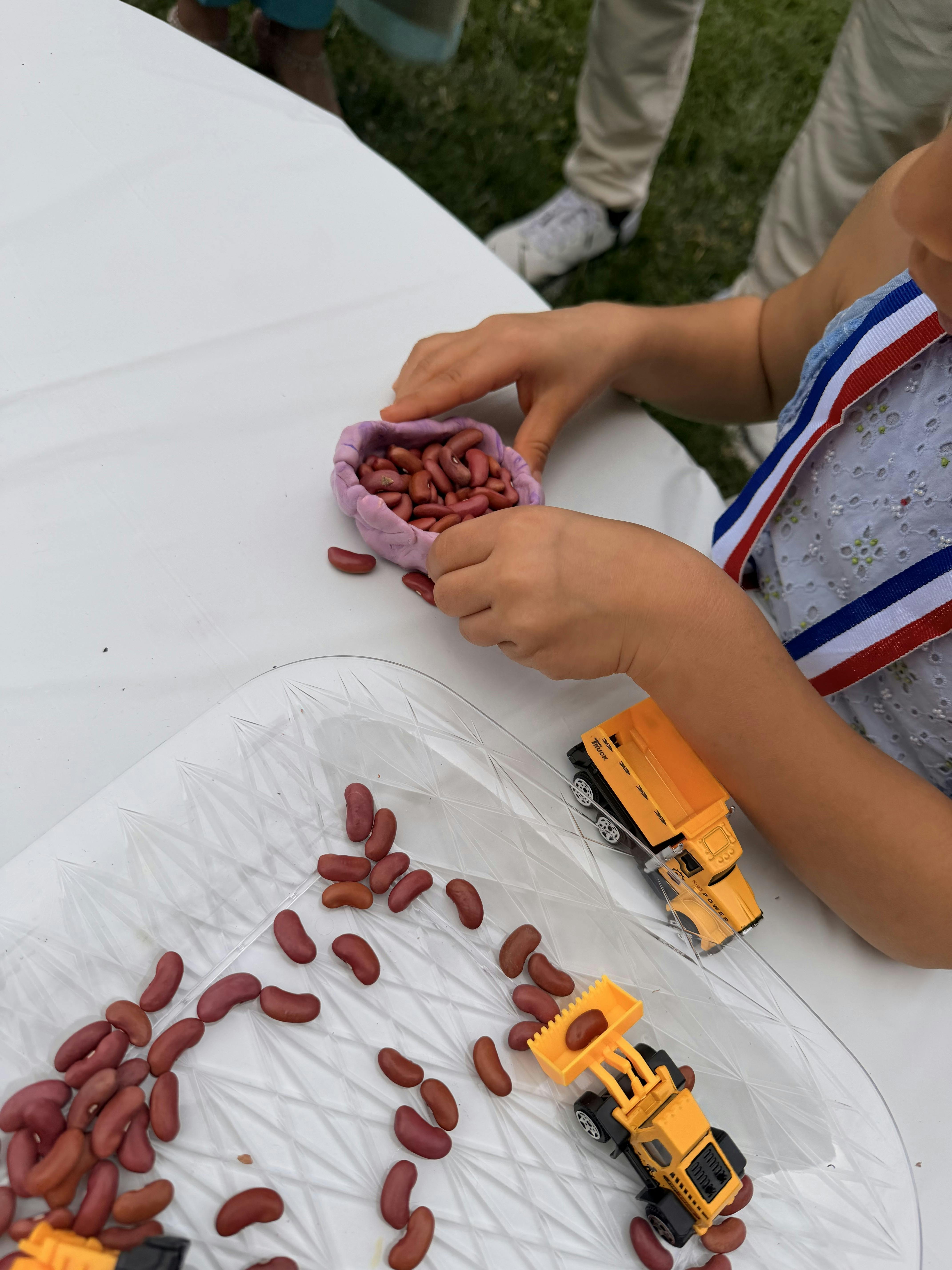 Child playing with kidney beans and toy construction vehicles on a table
