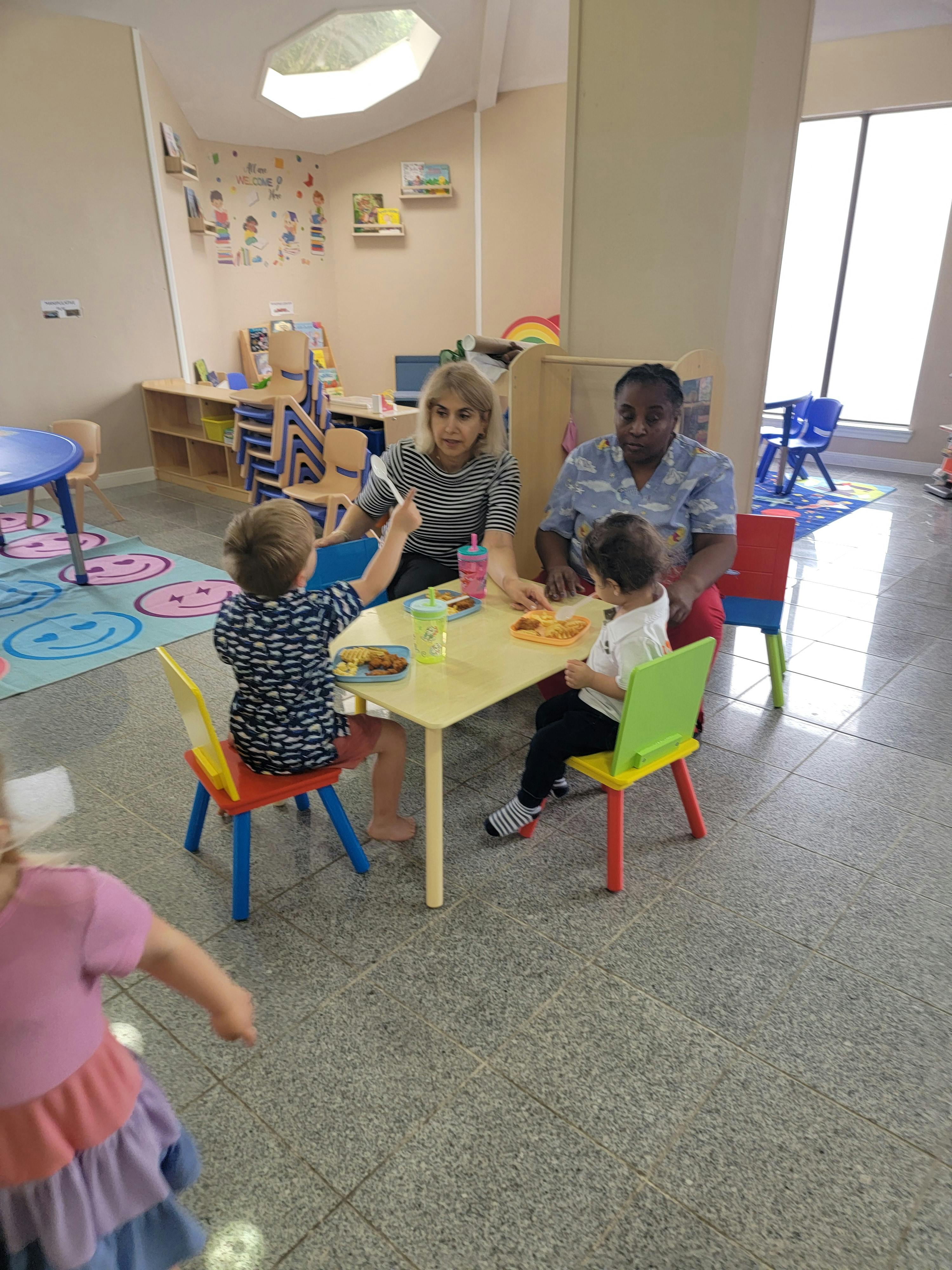 Two people and three children sitting at small tables in a classroom