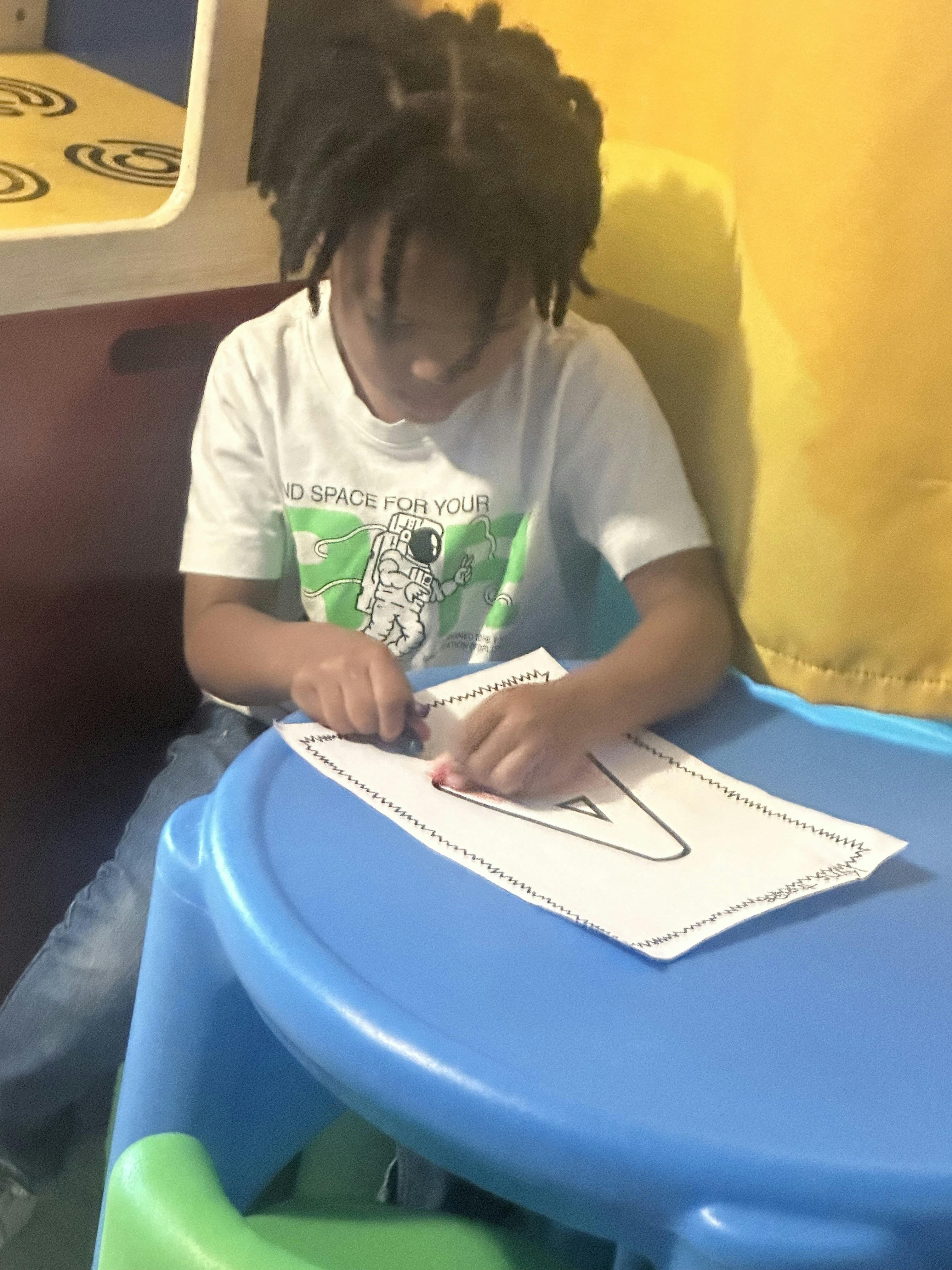 Child coloring the letter A on a sheet of paper at a small table