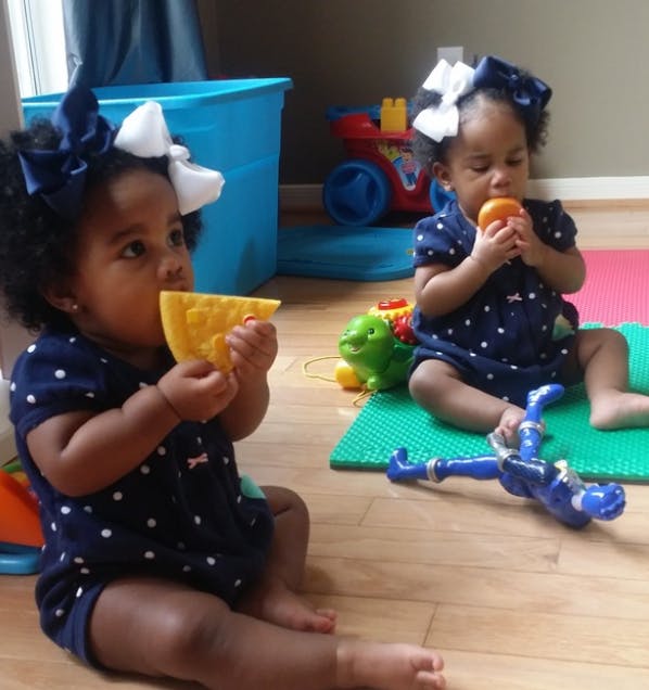 Two children sitting on the floor, one holding a yellow toy and the other an orange toy