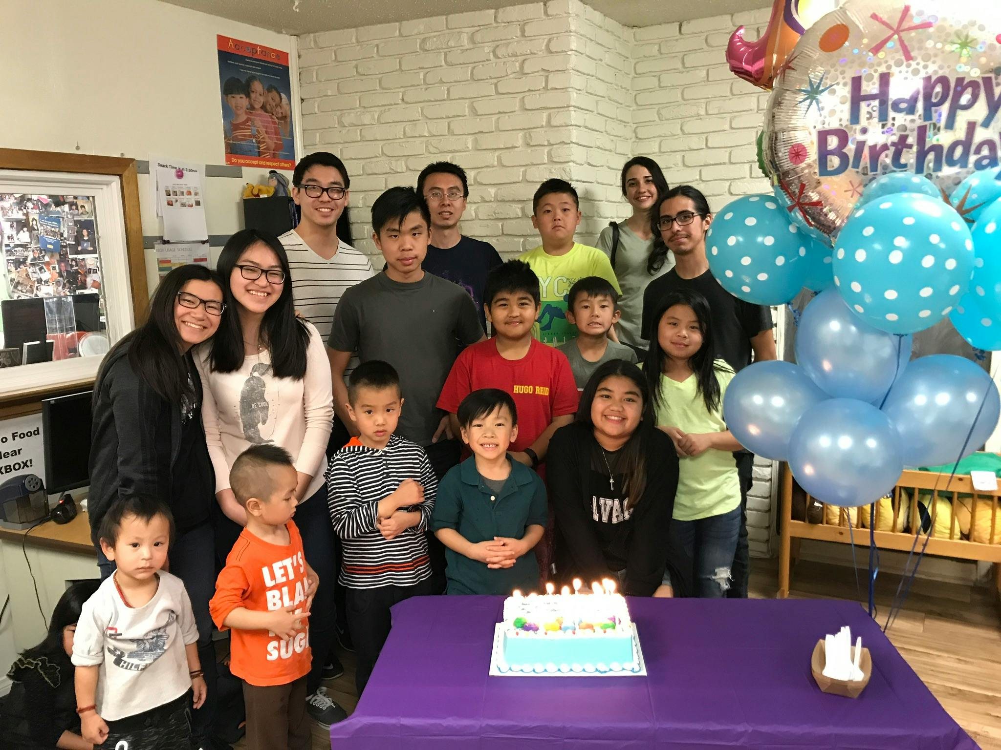 Group of people and children posing with a birthday cake and balloons
