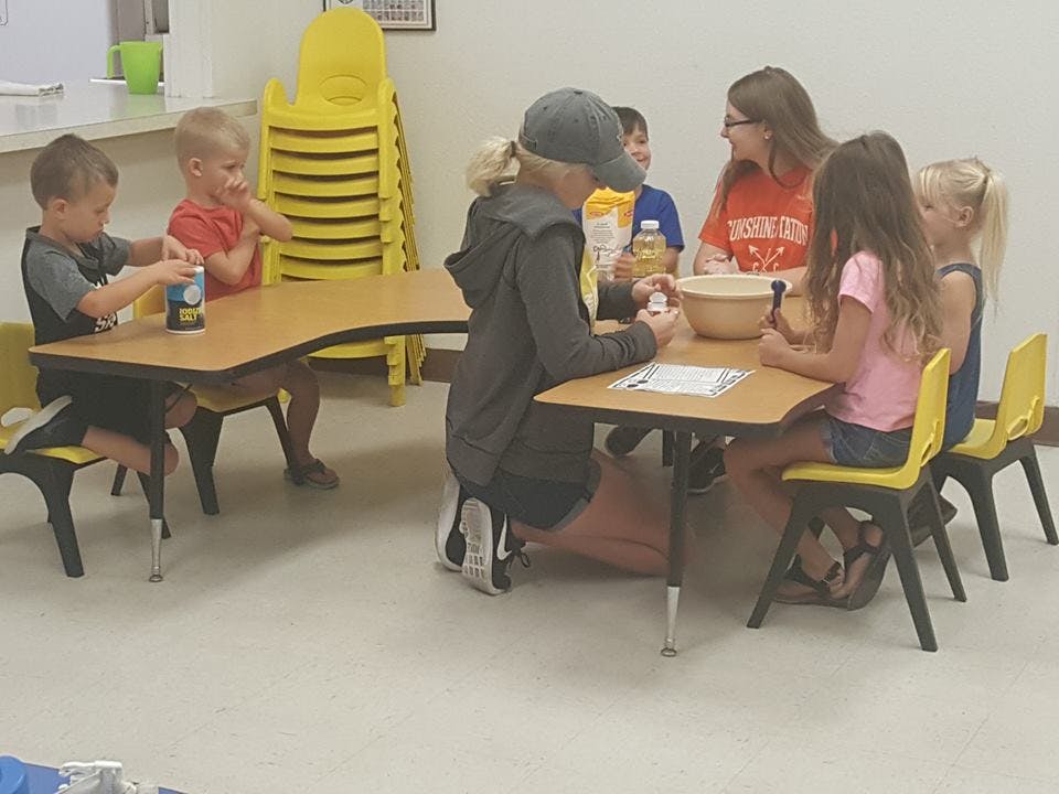 Adults and children at tables in a classroom