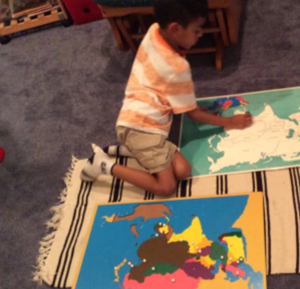 Child kneeling on a rug, working with a world map puzzle