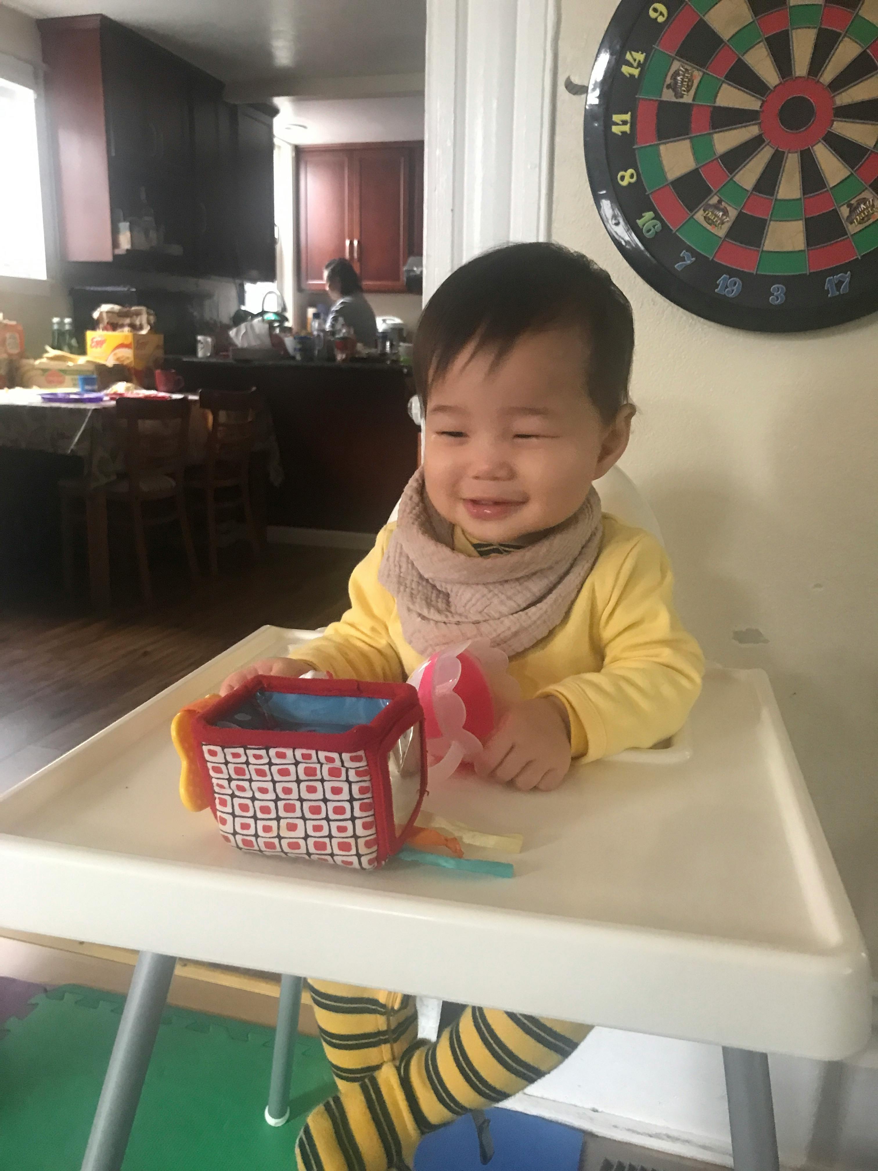 Child in a high chair with a toy and a dartboard in the background
