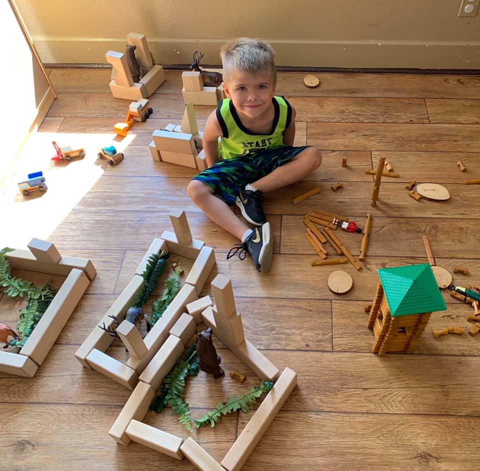 Child sitting on floor surrounded by wooden blocks and toys
