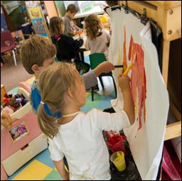 Child painting on an easel in a classroom with other children