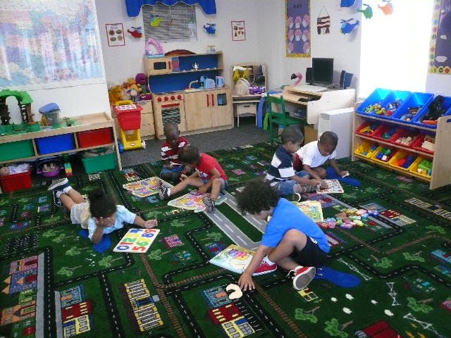 Children playing on a rug with roads and buildings in a classroom