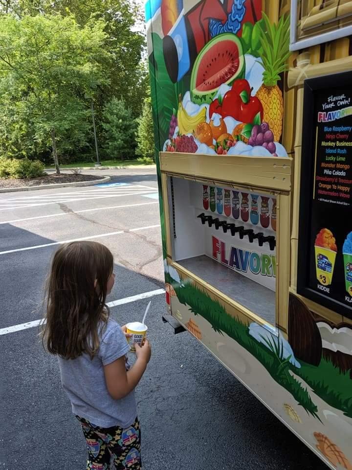 Child holding a cup with a spoon, looking at a food truck